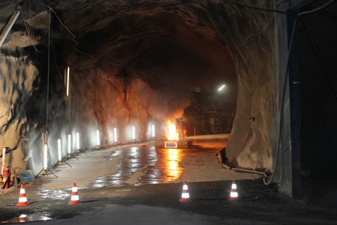 In der Mitte des Tunnels entsteht eine Stichflamme. Vorne schimmert der Boden, im Vordergrund stehen Pillonen.